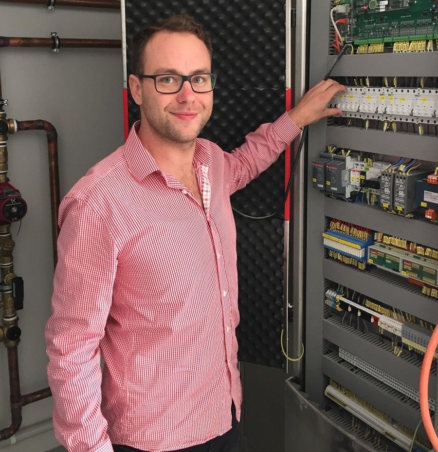 Phil Pacak, Euroheat engineer, standing beside a hydronic plant room control panel