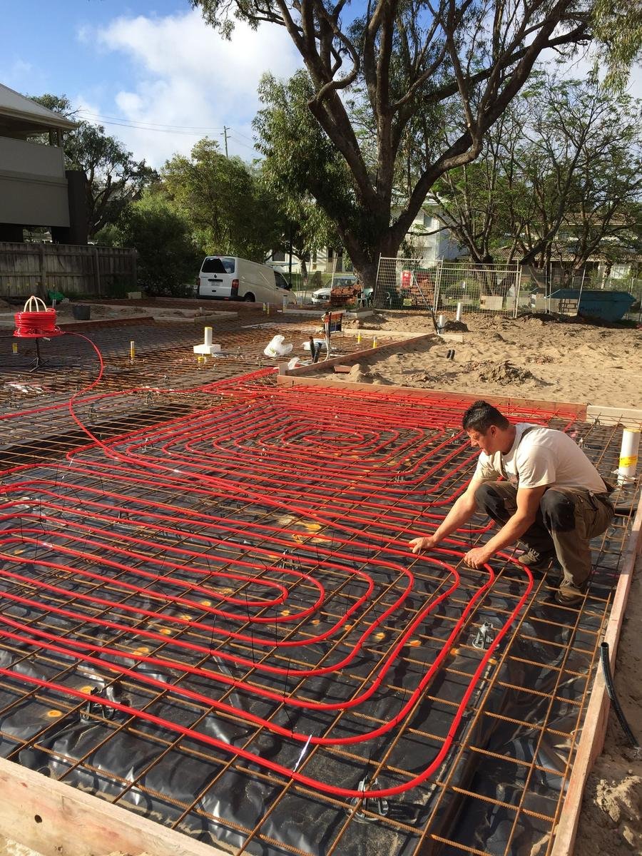 A Euroheat installer laying hydronic pipe loops across a residential slab before the pour, Perth new build