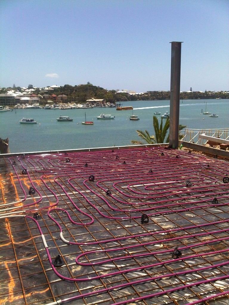Hydronic pipe loops laid on the reinforcing mesh of a suspended slab before the pour, marina behind